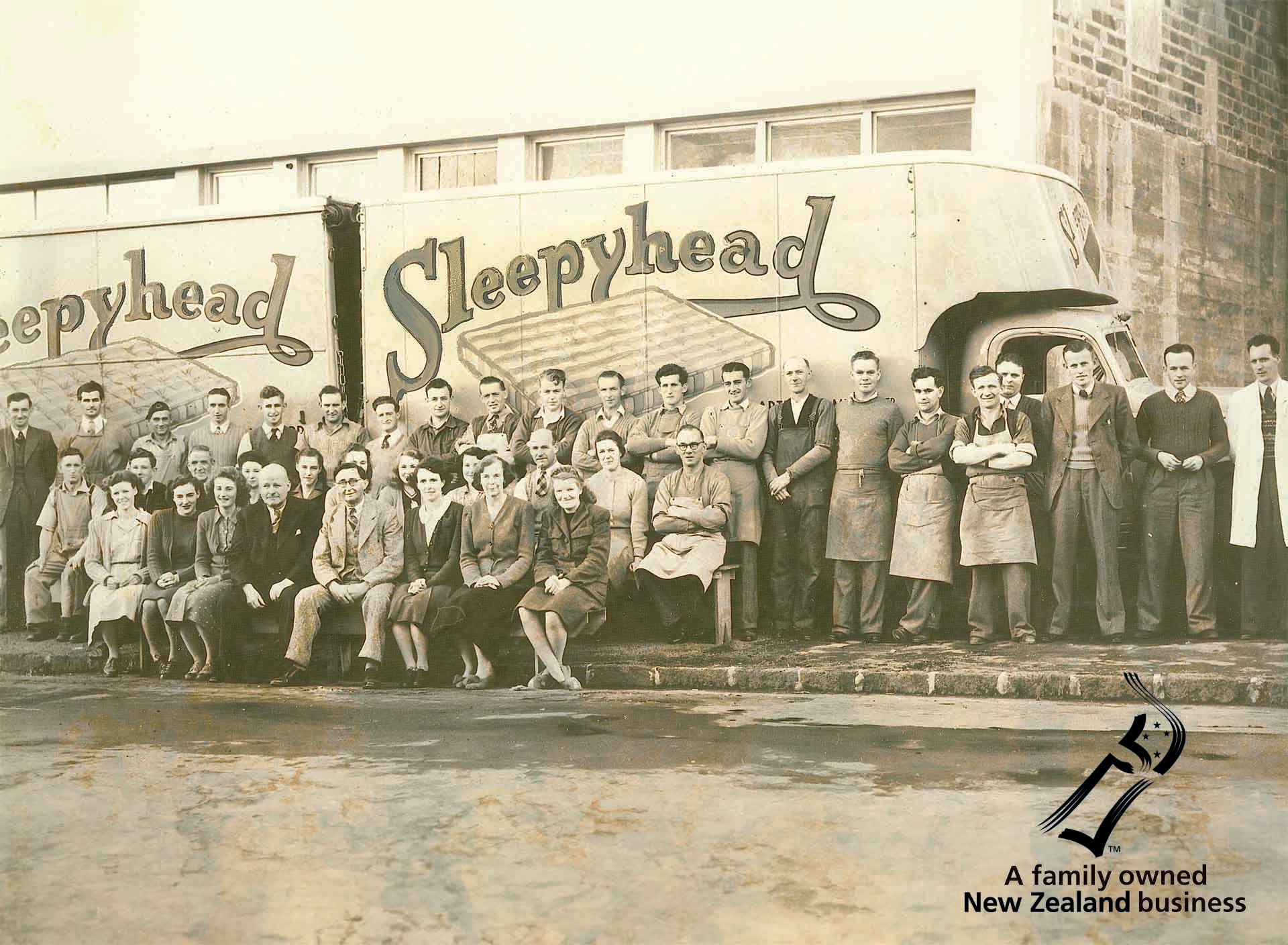 Group of people posing in front of a 'Sleepyhead' truck, with branding text overlay.