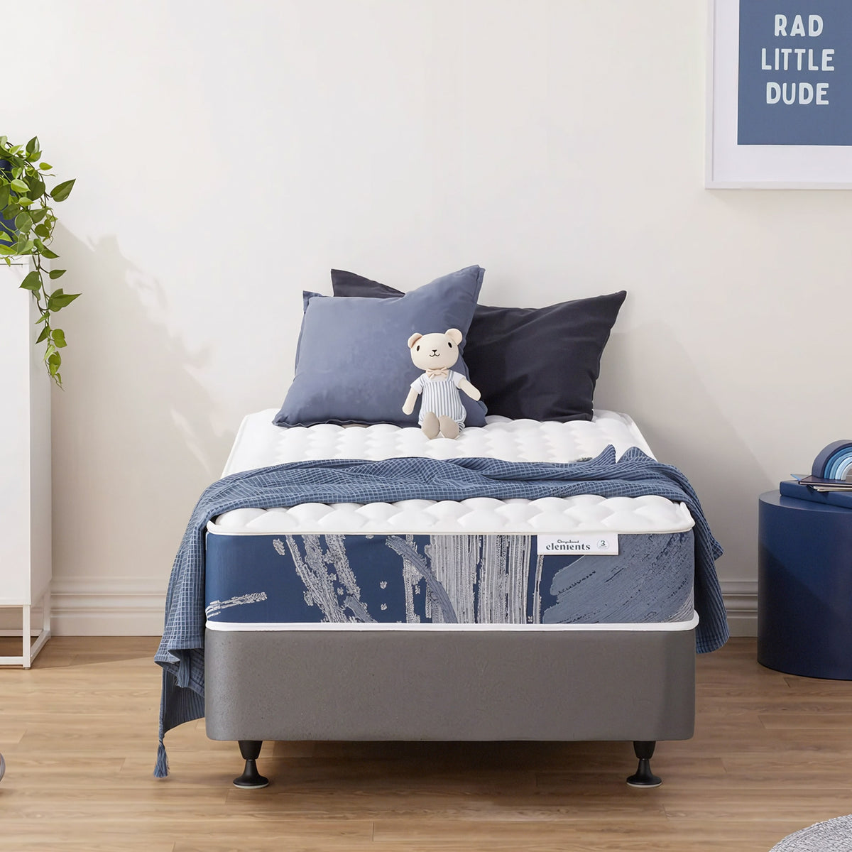Sleepyhead Elements bed with blue bedding and pillows in a room with a plant and framed picture.