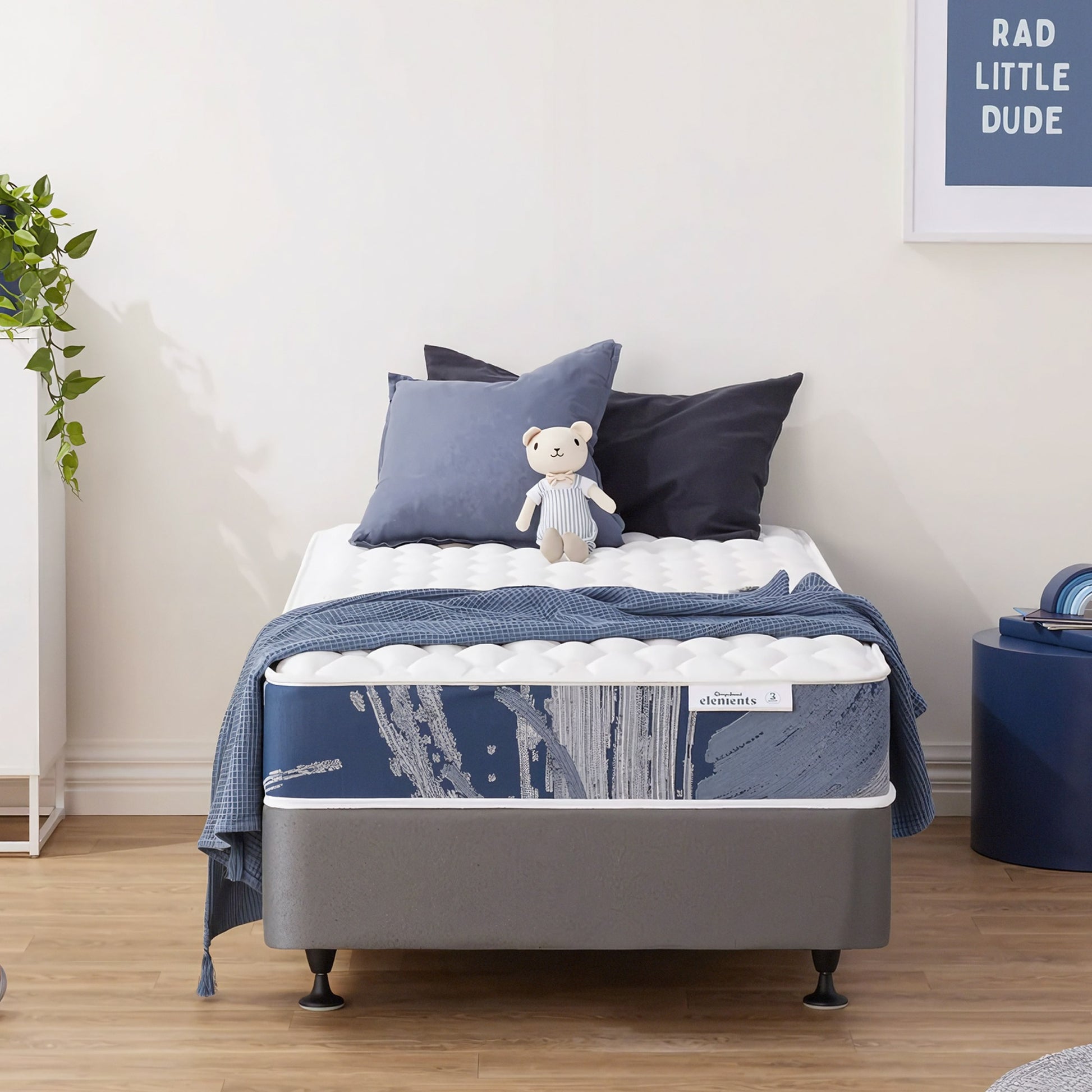 Sleepyhead Elements bed with blue bedding and pillows in a room with a plant and framed picture.